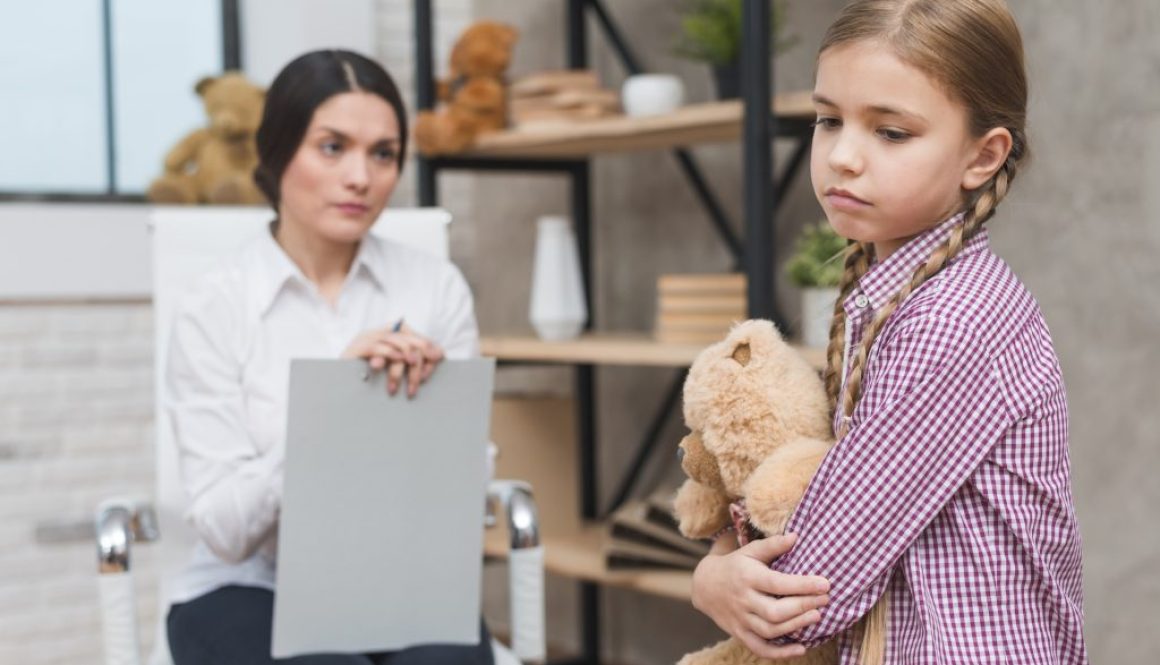 close-up-female-psychologist-looking-sad-girl-holding-teddy-bear