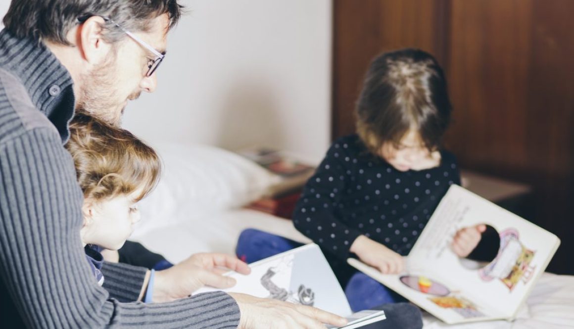 father-daughters-reading-books-bed